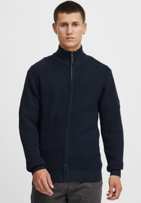 Mornarska zip-up dukserica, teksturirani pleteni materijal, visok ovratnik, rebraste manžetne i donji rub, uski kroj, sa malim logotipom na rukavu.
