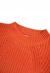 Oranssi neulepaita, jossa on ribbireunus kaula-aukossa, teksturoitu kuvio ja pehmeä, paksu kudonta. Ihanteellinen kerroksittain käytettäväksi viileämmässä säässä.