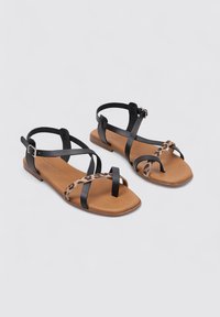 Sandalias de cuero negras con acentos de estampado de leopardo, suela plana, correas ajustables en los tobillos y bandas cruzadas. Adecuadas para uso casual.