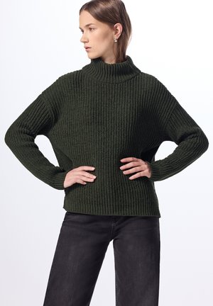 Donkergroen oversized trui met geribbelde textuur en een hoge kraag. Heeft verlaagde schouders en lange mouwen.