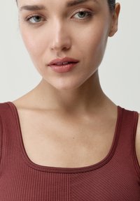 Detailný záber na osobu v bordovom rebrovom tielku s hranatým výstrihom, hladkou textúrou a jemným prešívaním.