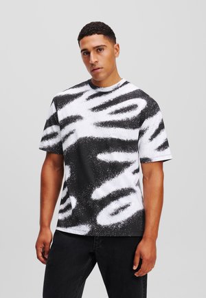 T-shirt a maniche corte bianco e nero con un motivo astratto di spray paint testurizzato. Collo rotondo e vestibilità rilassata.