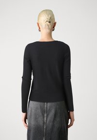 Svart langermet genser med bred rund hals, tettsittende design og ribbestrikket kant. Kombinert med et grått denimskjørt med en sentral søm.
