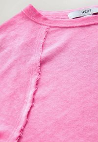 T-shirt rose en coton doux, doté d'un col rond et d'une couture à bords francs sur le côté, mettant en valeur une finition de tissu texturée.