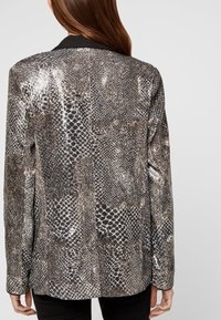 Metalický blejzr s stříbrným a černým hadím vzorem, s černým límcem a dlouhými rukávy. Hladká textura a přiléhavý střih.