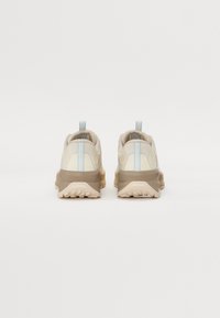 Zapatillas deportivas en color beige y marrón claro con una entresuela texturizada, que presenta una franja de acento azul claro y una lengüeta en el talón. Suela de goma resistente.