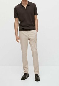 Donkerbruin poloshirt met korte mouwen, een halslijn en geribbelde manchetten, gecombineerd met beige op maat gemaakte broek en zwarte nette schoenen.