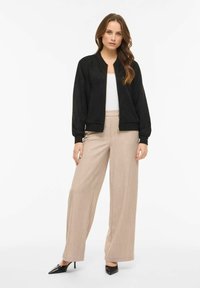 Juodas zomšos bombonešis su banguotais rankogaliais, derinamas su smėlio spalvos plačiomis aukštu liemeniu kelnėmis ir juodais smailiais bateliais aukštu kulnu.