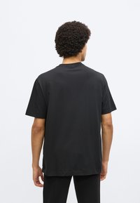 Čierne tričko s krátkym rukávom vyrobené z bavlny. Má klasický okrúhly výstrih a voľný strih. Hladká textúra bez viditeľných vzorov alebo log.