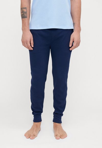 Navy blue fitted joggers with ribbed texture and gathered cuffs, made from a soft, stretchy fabric; worn with bare feet and a light blue shirt.