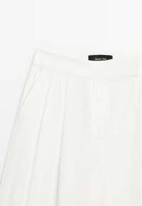 Bílé skládací kalhoty vyrobené z lehké tkaniny, s plochým pasem a bočními kapsami. Na pase je štítek značky "Massimo Dutti".