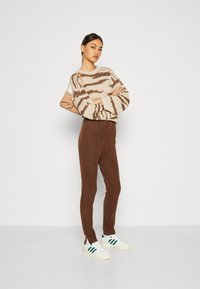 Strikkegenser med beige og brun abstrakt mønster, kombinert med brune slim-fit bukser og hvite sneakers med grønne striper.