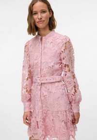 Robe en dentelle rose avec de longues manches bouffantes, motif floral, tissu semi-transparent, taille ceinturée et ourlet volanté.