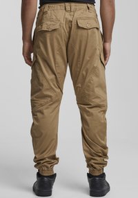 Kaki cargo hlače z elastičnimi manšetami, več žepi in sproščenim krojem. Izdelane iz lahkega materiala s gladko teksturo.