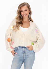 Cardigan lavorato a maglia di colore crema con appliqués floreali in arancione, rosa, viola e verde. Presenta un profondo scollo a V e due grandi bottoni.