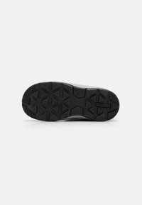 Semelle extérieure de sneaker noire avec un motif de grip texturé, comprenant des formes angulaires et un logo, conçue pour la durabilité et la traction.