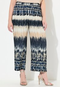 Plisserade vida byxor i marinblått, kräm och tan med tie-dye-mönster; elastisk midja; lätt tyg; kortad nederkant; bärs med sandaler med remmar.