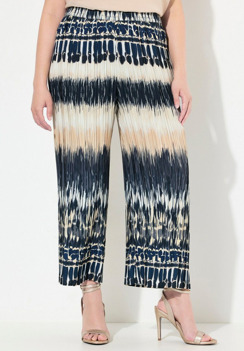 Plisserade vida byxor i marinblått, kräm och tan med tie-dye-mönster; elastisk midja; lätt tyg; kortad nederkant; bärs med sandaler med remmar.