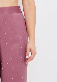 Pantalons en tissu mauve avec de petits motifs de cœurs argentés, dotés d'une taille plate et d'un design à jambe droite. Texture douce.