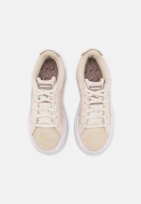 Baskets en daim beige avec semelles en caoutchouc blanc, lacets plats et une semelle intérieure marron texturée présentant un motif géométrique. Logo PUMA sur la languette.