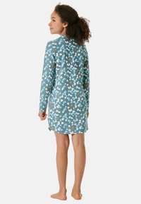 Nachthemd met lange mouwen in teal stof, voorzien van een bloemenpatroon met witte en gele accenten. Het is knielang met een licht gebogen zoom.