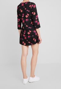 Schwarzes Kleid mit dreiviertel Ärmeln, floralem Muster in Pink und Grün, knielang, glattes Material, kombiniert mit weißen Sneakers.