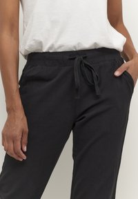 Schwarze Hosen aus Leinenmischgewebe mit elastischem Bund, Kordelzug-Detail, Seitentaschen und lockerem Schnitt. Strukturierter Stoff mit dezentem Glanz.