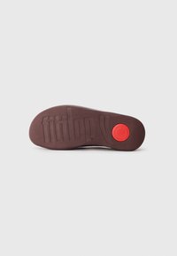 Semelle de chaussure en caoutchouc brun avec une surface texturée, arborant le nom de la marque "fitflop" en relief et un accent rouge circulaire près du talon.