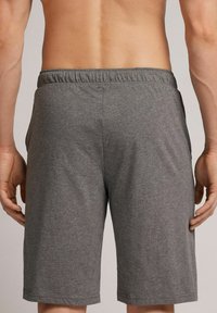 Graue Sportshorts aus weichem Stoff, mit einem elastischen Bund und seitlichen Taschen, die bis kurz über das Knie reichen.