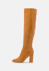 Bota de cuero brillante color bronce, hasta la rodilla, con punta afilada y tacón cuadrado. Diseño sin costuras y textura suave.