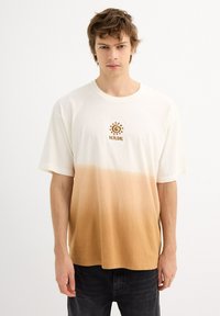 Camiseta de manga corta con degradado en blanco que se desvanece a marrón claro, con un diseño de sol y espiral en marrón en el pecho. Material de algodón suave.