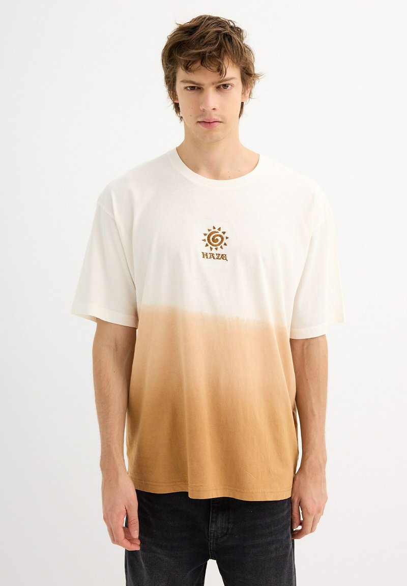 Camiseta de manga corta con degradado en blanco que se desvanece a marrón claro, con un diseño de sol y espiral en marrón en el pecho. Material de algodón suave.