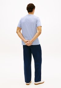 Ριγέ κ οντομάνικη μπλούζα σε ανοιχτό γαλάζιο και λευκό, σε συνδυασμό με ναυτικό παντελόνι φαρδύ και λευκά αθλητικά παπούτσια, εμφανιζόμενα από πίσω.