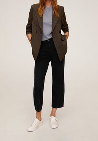 Dvojřadý olivový blazer s jemnými pruhy přes světle šedé tričko, v kombinaci s vysokými černými zkrácenými džíny a bílými teniskami.