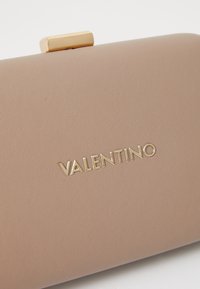 Beige texturerad Valentino clutchväska med gyllene logotypbokstäver och en gyllene rektangulär lås på toppen.