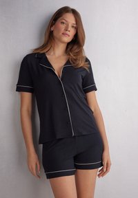 Navy-kleurige katoenen mix korte pyjama's met een kortemouwige knoopshirt met witte piping en bijpassende shorts met een vergelijkbare afwerking.