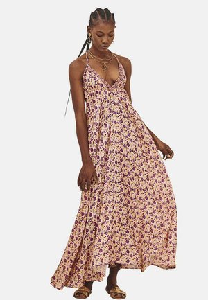 Vestido maxi de tela rosa claro con patrón floral púrpura, escote en forma de V y tirantes finos; silueta fluida hasta los tobillos.