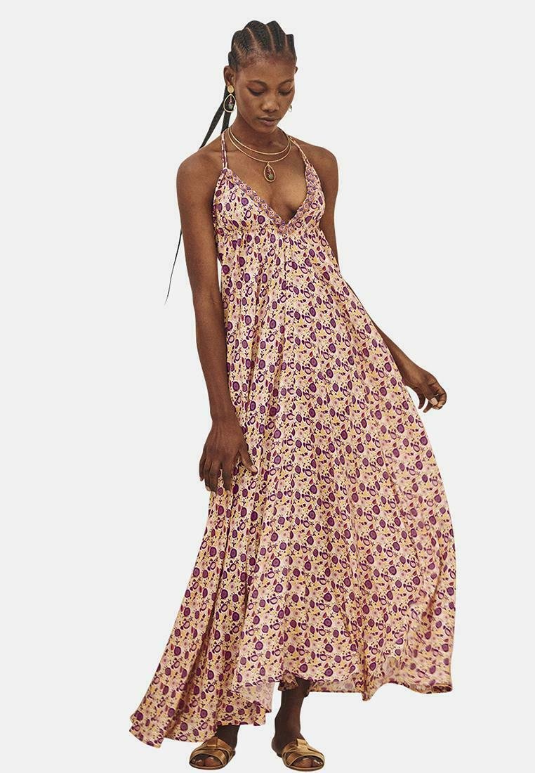 Vestido maxi de tela rosa claro con patrón floral púrpura, escote en forma de V y tirantes finos; silueta fluida hasta los tobillos.
