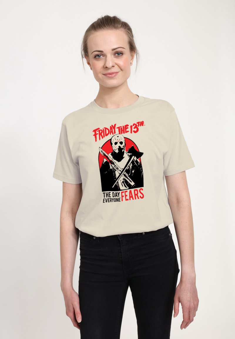 Cremefarbenes T-Shirt mit einer Grafik einer maskierten Figur, die Waffen hält, rotem Kreis im Hintergrund und dem Text "Freitag, der 13." sowie "DER TAG, VOR DEM ALLE ANGST HABEN."