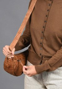 Bolso cruzado de textura marrón con una correa suave y un bolsillo con cremallera. La superficie presenta un patrón único en espiral. Se lleva con un cárdigan marrón.