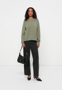 Olijfgroene sweatshirt met ronde hals, gecombineerd met donkergrijze wijde broek. Zwarte handtas met gouden hardware en puntige hakken.