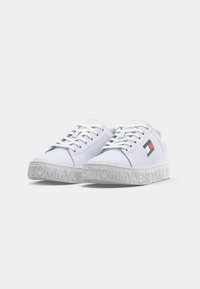 Baskets blanches basses avec lacets, arborant le logo Tommy Jeans sur le côté et une marque en relief sur les bords de la semelle.