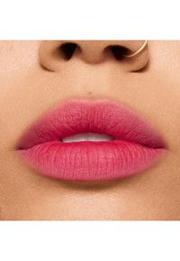 Gros plan sur des lèvres roses à texture mate, présentant un dégradé allant du rose clair au rose foncé. Teint naturel visible autour des lèvres.