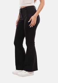 Pantaloni neri a zampa d'elefante in tessuto elasticizzato, con vita alta e cuciture laterali. Abbinati a sneakers bianche per un look casual.