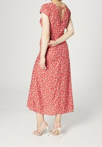 Vestido midi rojo con flores, mangas cortas abullonadas, detalle de espalda con ojal y una silueta fluida. Combinado con tacones altos blancos con tiras.
