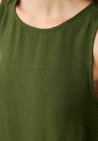 Zielony bezrękawnik wykonany z teksturowanej tkaniny, z okrągłym dekoltem i minimalistycznym designem, podkreślający gładkie, matowe wykończenie.