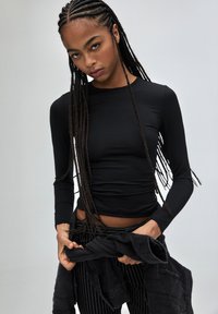 Top negru cu maneci lungi, cu un design ajustat, textură netedă și decolteu rotund, asortat cu pantaloni în dungi negre și albe.