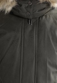 Olivgrön parkas med fuskpälsfoder i huvan, har en dragkedja fram, tryckknappar och ribbade sömdetaljer. Mjuk och vattentålig tyg.