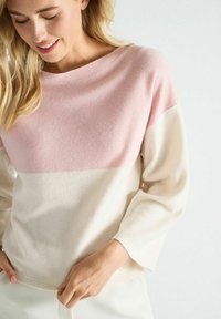 Pull léger à col rond, présentant une partie supérieure rose et un bas crème. Texture douce, manches longues et coupe décontractée.