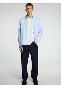 Svetlo modra prugasta srajca s gumbi čez belo majico, v kombinaciji z temno modrimi kavbojkami in črnimi čevlji. Preprost dizajn in sproščen kroj.